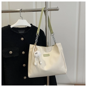 Detail of cream tote bag with green strap, fashion label, and cute fuzzy charm
