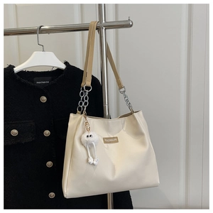 Close-up of beige tote bag with chain strap and cute plush monster charm detail