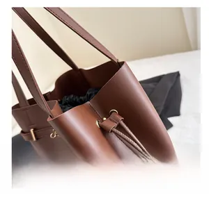Close-up of brown leather tote bag detailing premium metal buckles and black drawstring liner
