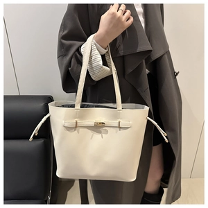 Detail of a creamy white leather tote bag featuring a gold twist lock and side drawstrings