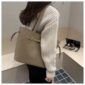 Detail of a large khaki bucket bag with side drawstring and metal buckle on model