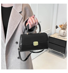 Close-up of matte black leather handbag with gold buckle and top handle details