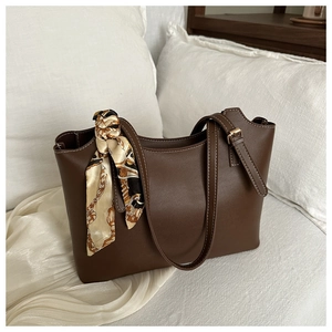 Detail of dark brown leather tote bag with elegant silk scarf on handle and gold buckle