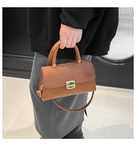 Detail of brown leather handbag featuring suede flap and golden square buckle on model
