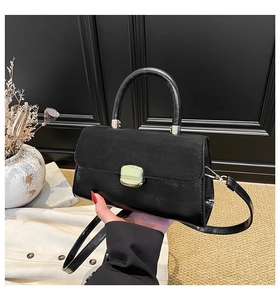 Close-up of black crossbody bag with suede texture, gold hardware and hard handle