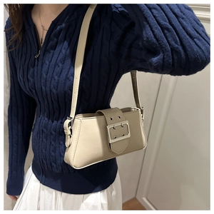 Detail of a beige Y2K baguette bag with silver buckle worn over a navy knit sweater