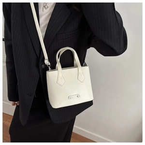Detail of cream white leather bucket bag showing adjustable strap and dual handle design