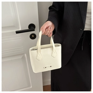 Detail of a creamy white mini bucket bag featuring a polished metal fashion plaque