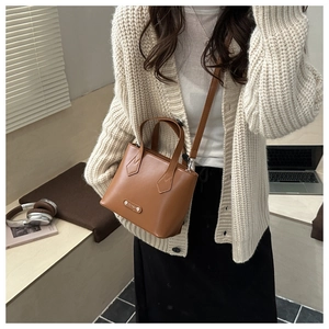 Detail showing a stylish caramel brown leather bucket bag with top handles and logo