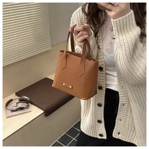 Detail of caramel leather handbag with gold logo plaque in a cozy lifestyle setting
