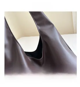 Gros plan des coutures fines et du cuir mat marron foncé sur un grand sac cabas