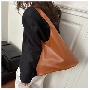 Vue latérale d'un grand sac cabas en cuir caramel porté par un mannequin en studio