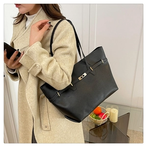 Detail of large black leather tote bag with gold buckle worn with a beige coat