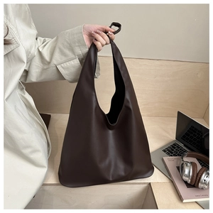 Vue détaillée du sac cabas en cuir mat marron foncé avec un trench-coat beige