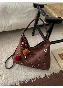 Detail of dark brown suede hobo bag with silver grommets and colorful pompom charms