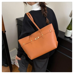 Detail view of a brown leather tote bag with gold swivel lock on a female model shoulder