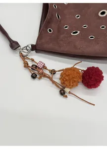 Detail of brown suede tote bag with metal eyelets and bohemian handmade tassel charm