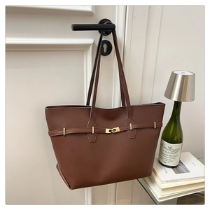 Close-up of a brown tote bag with gold hardware detail hanging on a white door
