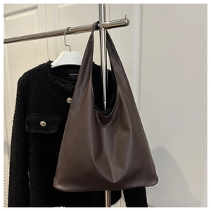 Détail d'un grand sac cabas en cuir marron foncé sur support avec veste en tweed