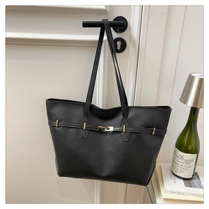 Detail of minimalist black leather tote bag with gold buckle and slim straps on a door