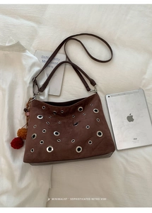 Detail of dark brown suede tote bag with silver eyelets and colorful fur pompom charm