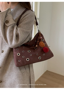 Detail of vintage suede tote bag with metal eyelets and decorative plush ball charms