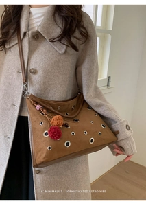 Close-up of brown suede tote bag with silver grommet details and a fuzzy pom-pom charm