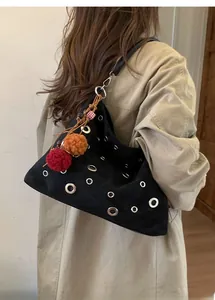 Detail of black suede tote bag with silver metal grommets and colorful fuzzy pom-pom charms