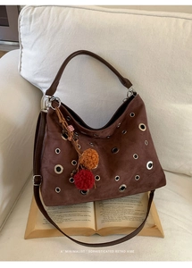 Detail of brown suede tote bag with metal grommets and retro charm on a book