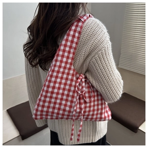 Detail of red and white gingham tote bag with side ribbons worn over a beige sweater