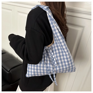 Detail of blue and white checkered tote bag with a bow tie strap on a model shoulder