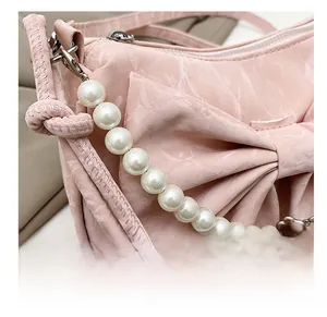 Dettaglio borsa rosa con fiocco, trama satinata e manico decorativo in perle sintetiche