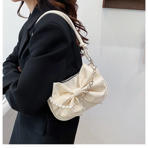 Dettaglio borsa color crema con fiocco e tracolla di perle su blazer nero