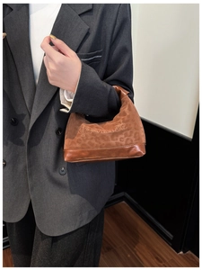 Detail of leopard print dumpling bag with brown leather base held by a model in a suit