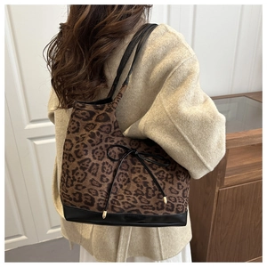 Detail of leopard print tote bag featuring black leather straps and a decorative bow tie