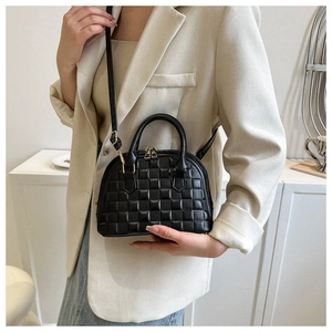 Detail of black shell-shaped handbag with checkered embossing and gold hardware strap