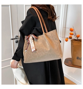 Close-up of matte beige tote bag featuring thin brown handles and silk scarf detail