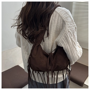 Detail of dark brown suede shoulder bag with tassels shown on a model for draping effect