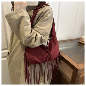 Detail of burgundy suede hobo bag featuring long bohemian tassels and matte texture