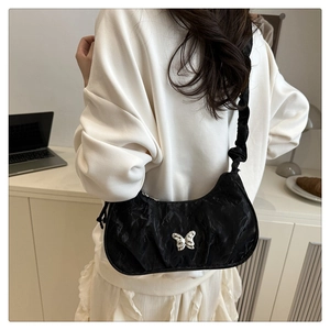 Dettaglio di borsa a spalla plissettata nera con farfalla d'argento in stile minimalista