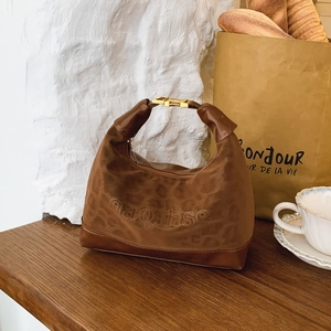 Brown leopard print crescent hobo bag made of suede leather on a rustic wooden table
