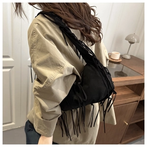 Detail showing long black fringes and textured strap on a slouchy shoulder tote bag