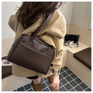 Detail of dark brown vintage PU leather shoulder bag worn over a beige trench coat