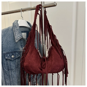 Detail of burgundy hobo tote bag with long tassels hanging against a denim jacket