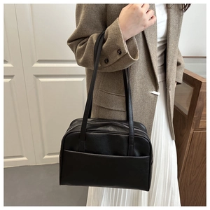 Detail of black PU leather shoulder bag with dual zippers and front pocket on a model