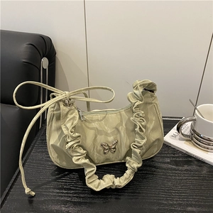 Borsa a spalla plissettata verde chiaro con ciondolo a farfalla su tavolo di legno scuro
