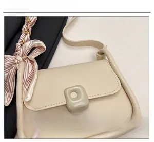 Close-up of cream crossbody bag with square metal buckle and pink silk scarf bow detail