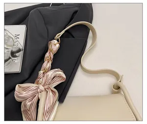 Detail of beige crossbody bag strap wrapped with a striped silk scarf and bow