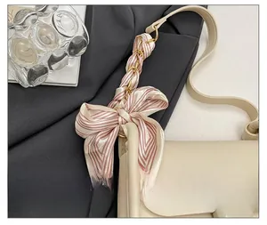 Detail view of beige leather shoulder bag featuring a pink striped silk scarf on the strap