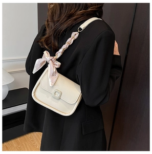 Creamy white shoulder bag with silk scarf chain strap worn by model in black suit